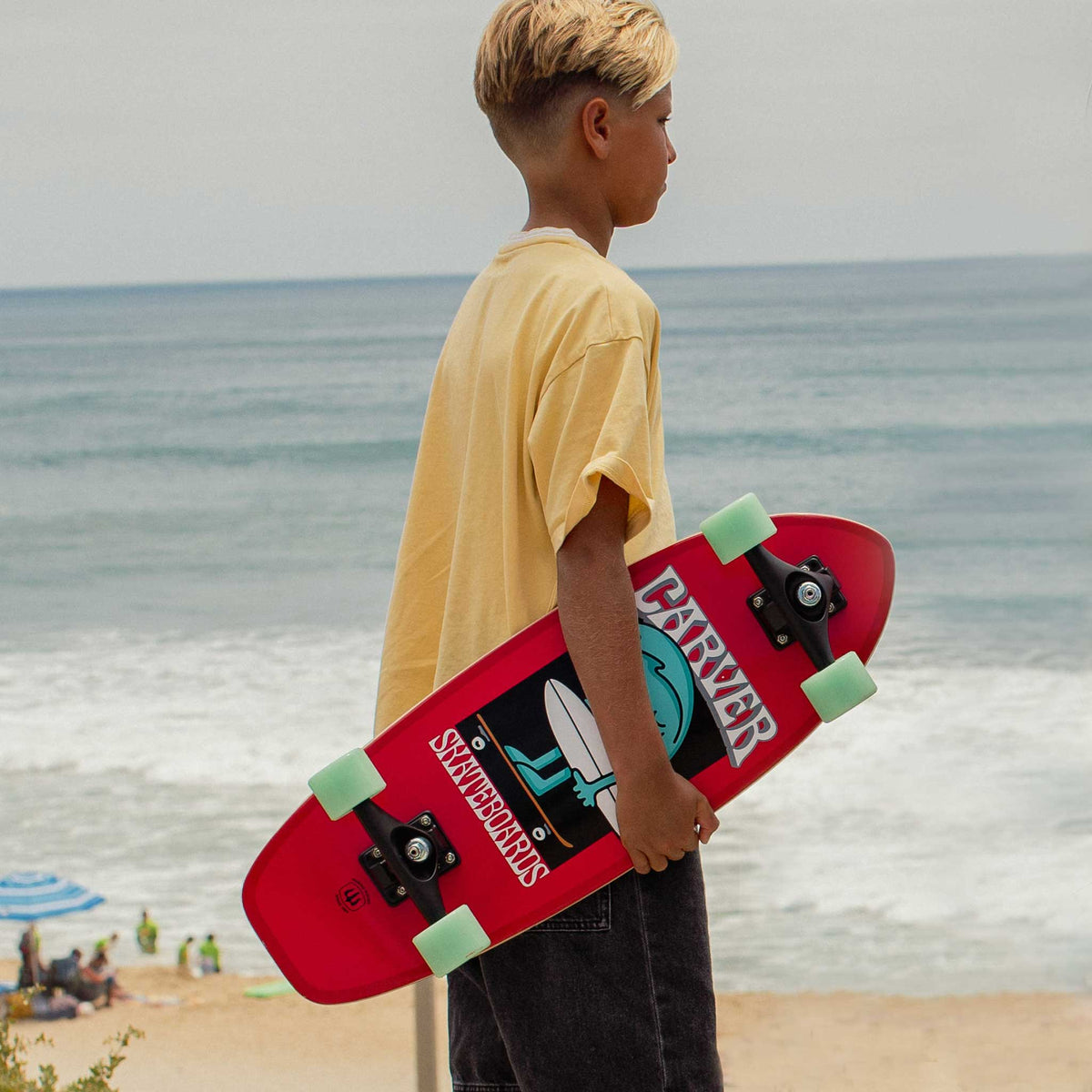 Enfant tenant un surfskate Carver Wavy Davy face à la plage